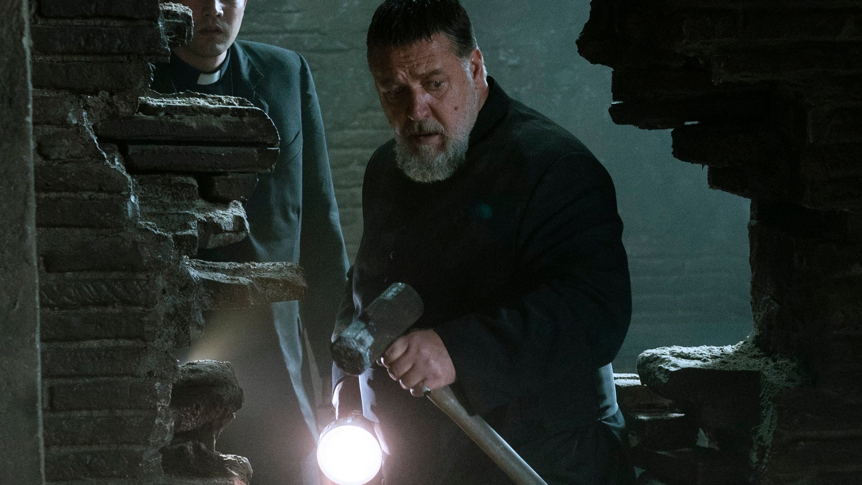 russell crowe as a priest, having just broken down a brick wall with a hammer